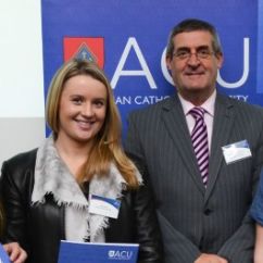 Young woman standing next to middle-aged man in front of ACU banner