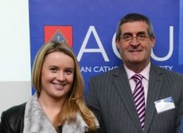 Young woman standing next to middle-aged man in front of ACU banner