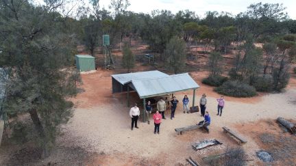 A birds eye view of Earthwatch fellows standing in bushland near a hut with a corrugated roof..