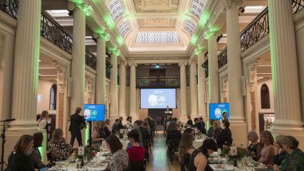 Guest at teh dinner seated at rectangular tables down the length of the Queen's Hall with large screens at the end.