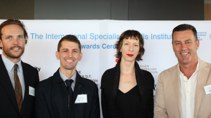 Four people standing shoulder to shoulder and smiling in front of a media wall. 