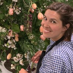 Aga Jones, ISSI fellow and sustainable florist. Woman smiling in front of a large floral arrangement of white and orange flowers. 