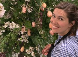 Aga Jones, ISSI fellow and sustainable florist. Woman smiling in front of a large floral arrangement of white and orange flowers. 