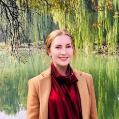 Georgia McDonald, Griffith University Scholar. Young woman wearing a red top smiling and standing in front of a lake.