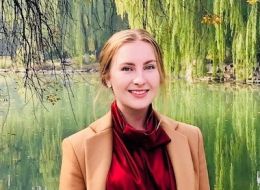 Georgia McDonald, Griffith University Scholar. Young woman wearing a red top smiling and standing in front of a lake.