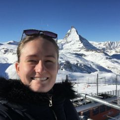 Simone De Nys, ANU scholar. Blonde woman with a black fluffy jacket standing in front of a snowy mountain range.