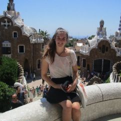 Yougn woman sitting on a low wall overlooking Gaudi buildings in Barcelona