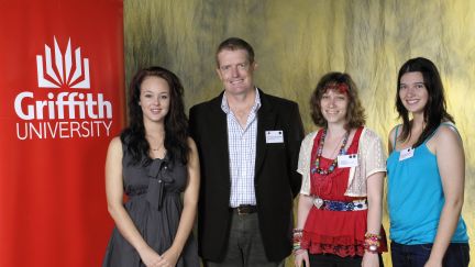 Three young female GAF scholars with GAF representative next to Griffith Uni banner