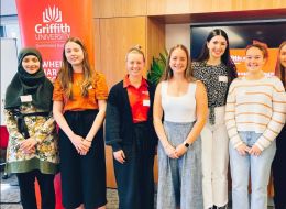 Seven female scholars standing in front of a Griffith Uni banner