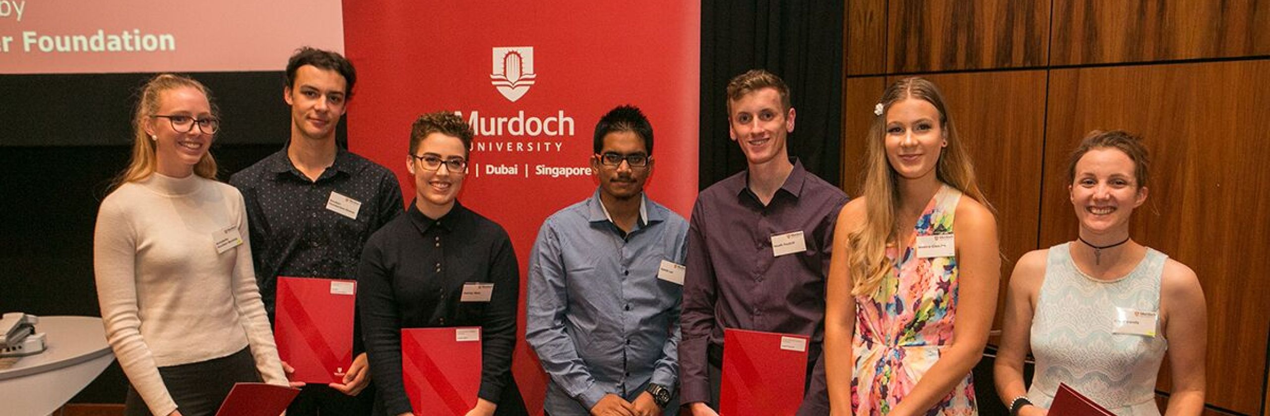 Three female and four male scholars in front of Murdoch banner