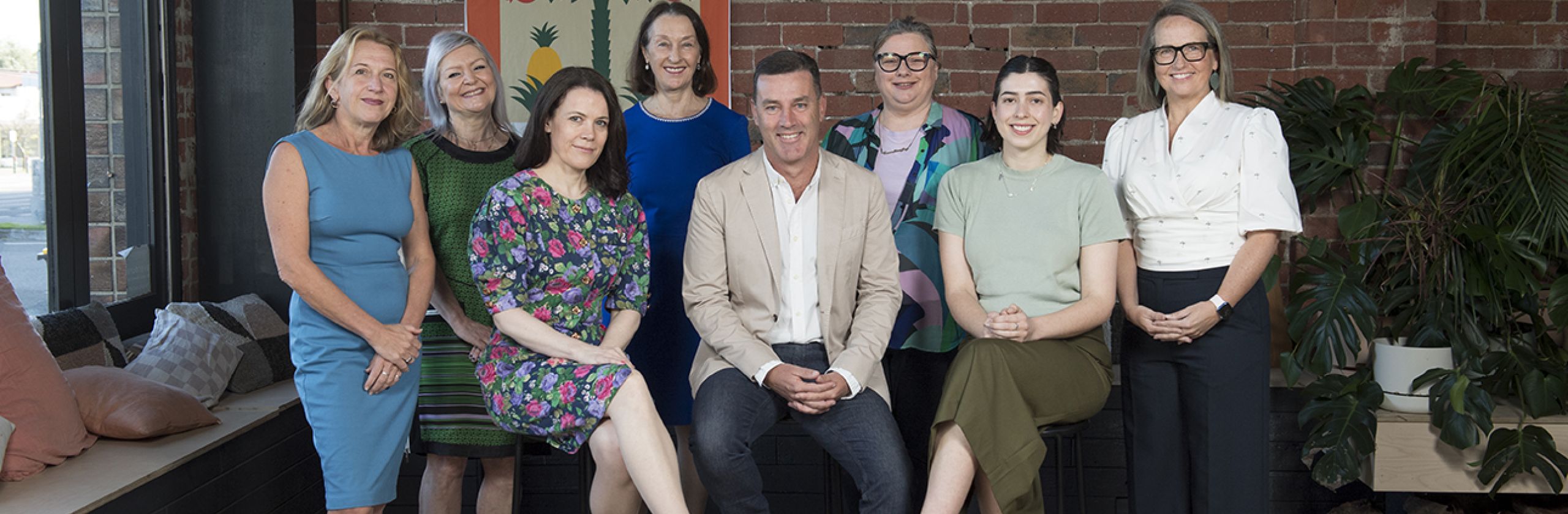 The George Alexander Foundation staff group. Eight people sitting and standing with a red brick wall in the background. 