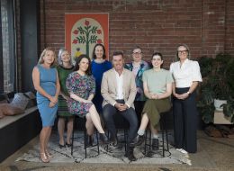 The George Alexander Foundation staff group. Eight people sitting and standing with a red brick wall in the background. 