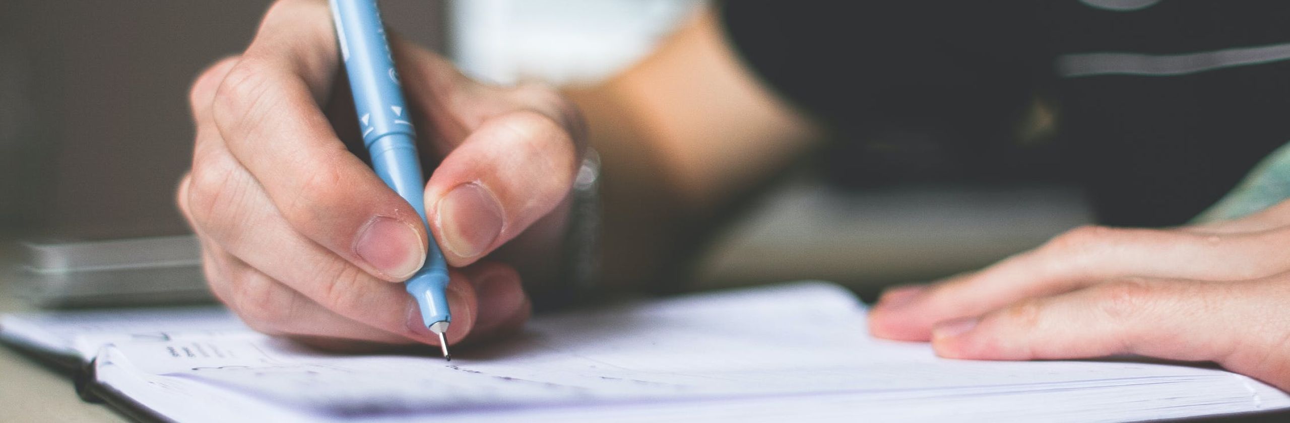 Up close view of a hand holding a pen and writing in a journal