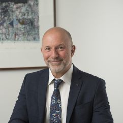 Middle-aged man in suit and tie sitting at desk smiling