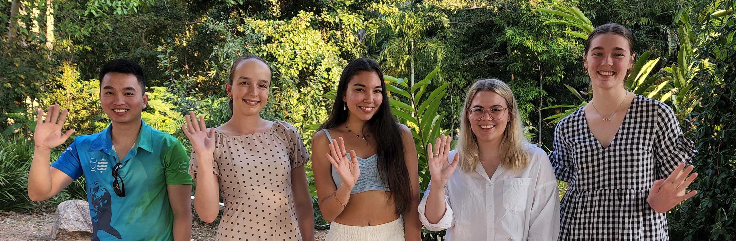 Five James Cook University scholars waving, standing outside with trees and plants in the background.