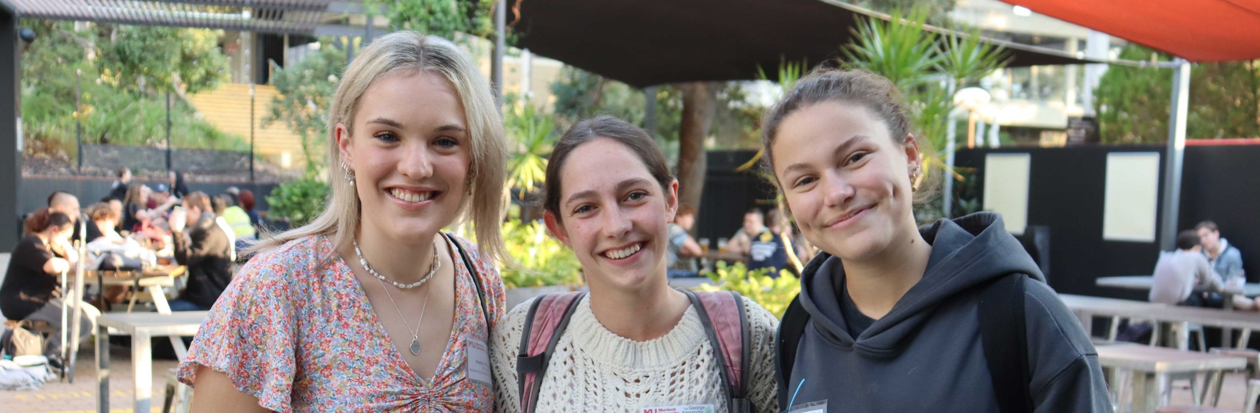 Three young people smiling with their arms linked and standing outside.