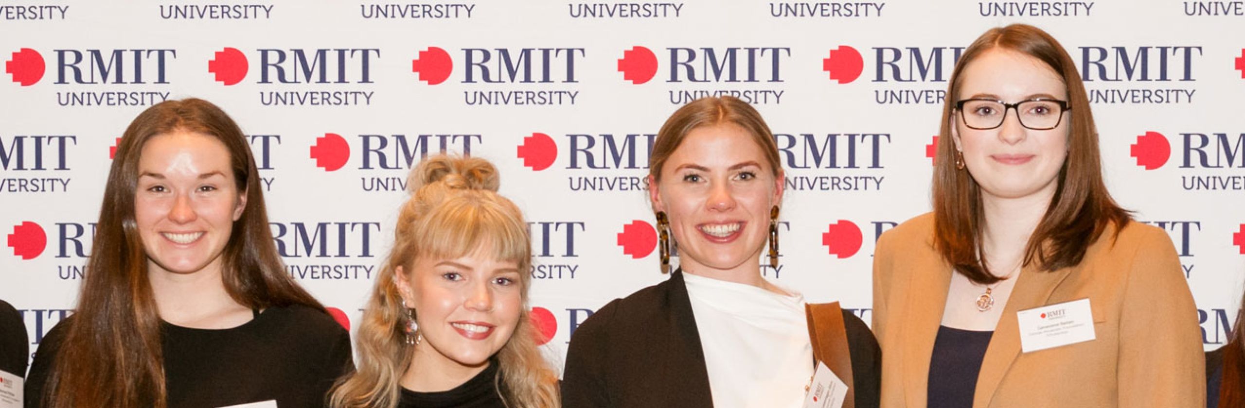 A group of RMIT Scholars smiling in front of a banner with the RMIT logo. 