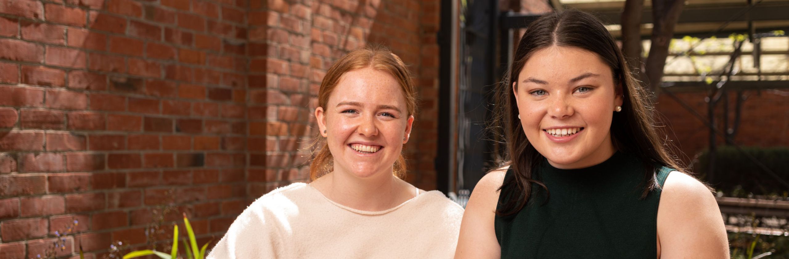 Two UniSA Scholars smiling and sitting outside at a wooden table. 