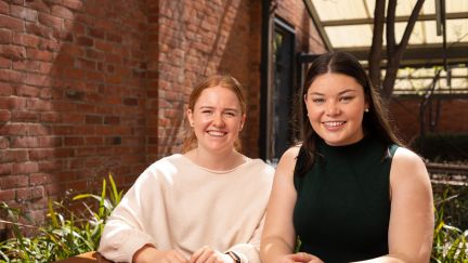 Two UniSA Scholars smiling and sitting outside at a wooden table. 