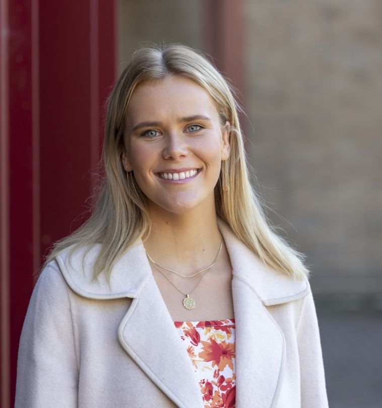 Blonde university student smiling, standing outside.