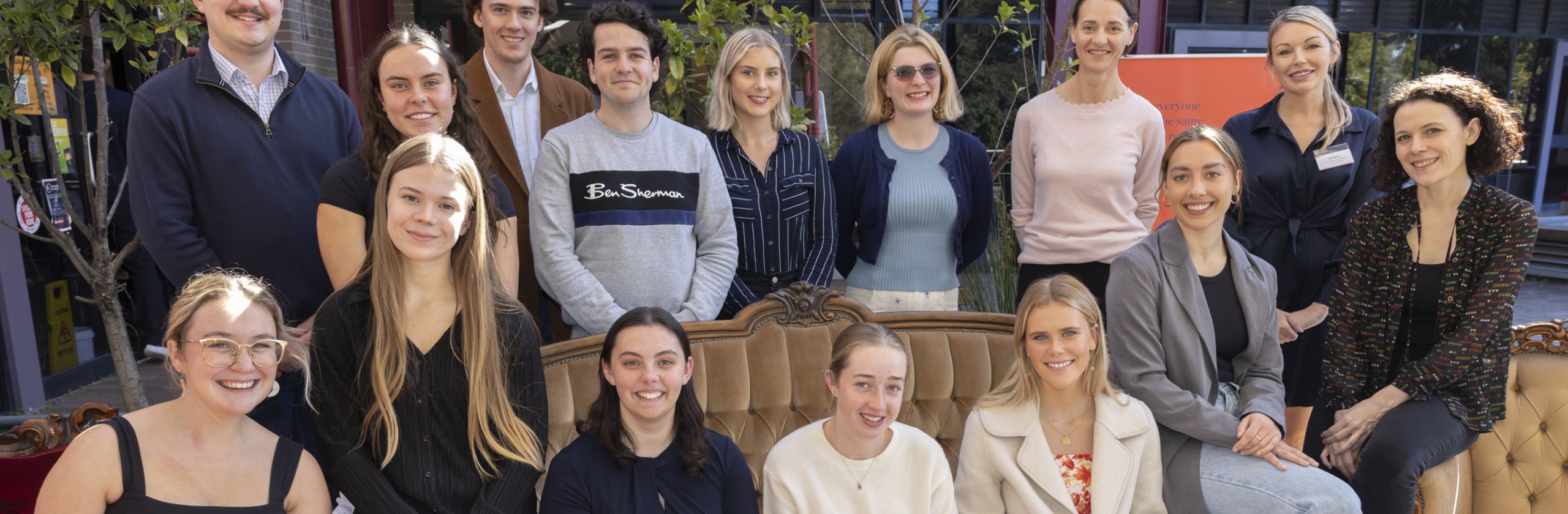 A large group of students sitting on a couch outside and smiling.