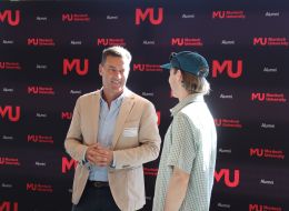 GAF CEO Paul Conroy speaking with a student whose back is turned away from the camera, set against a Murdoch Uni logo-filled background.