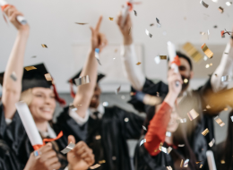 Picture of graduating crowd in graduation gear amongst confetti.